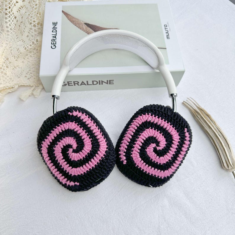 May include: White headphones with black and pink crocheted earmuffs featuring a spiral pattern.