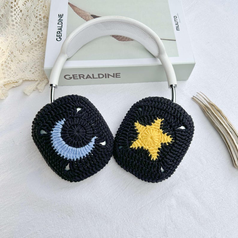 May include: White headphones with black crocheted ear covers. One ear cover has a blue crescent moon and the other has a yellow star.