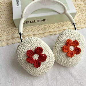 Puede incluir: Fundas para auriculares de crochet blanco con un dise&ntilde;o de flores rojas y naranjas.