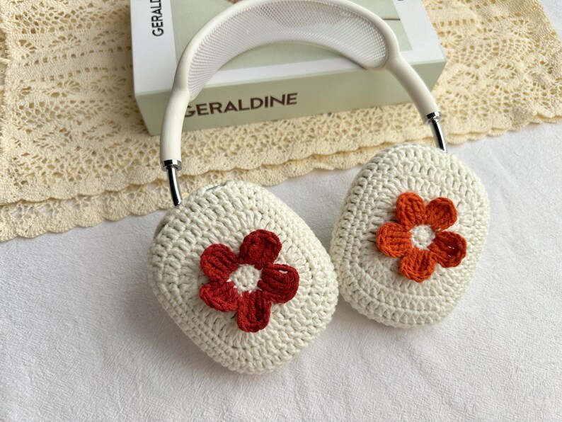 Puede incluir: Fundas para auriculares de crochet blanco con un dise&ntilde;o de flores rojas y naranjas.