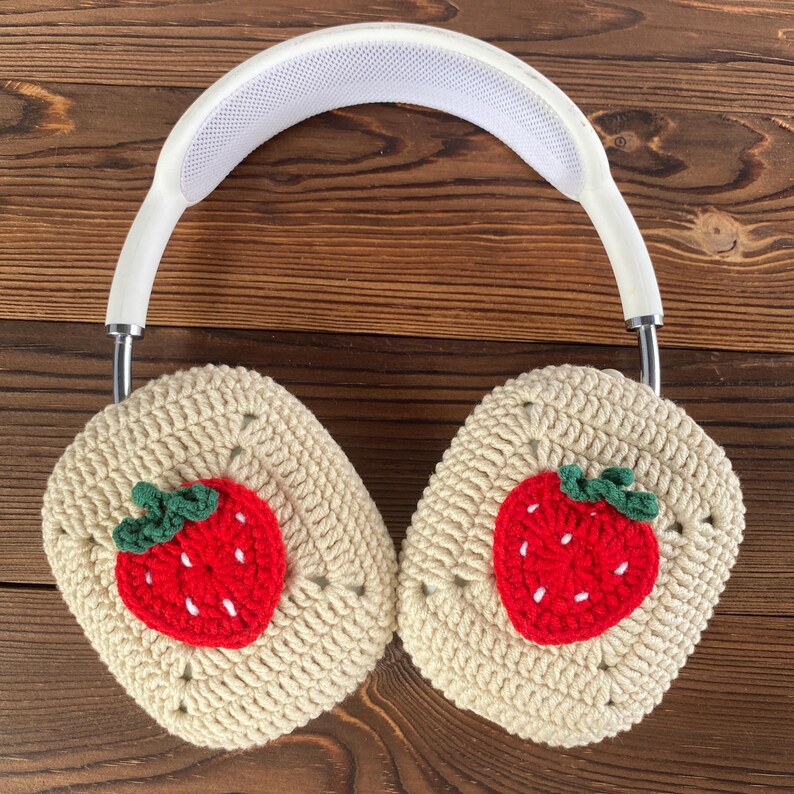 May include: White headphones with crocheted earmuffs featuring embroidered strawberry designs. The earmuffs are beige with red and green strawberries.