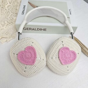 May include: White crocheted headphone covers with pink crocheted hearts. The covers are designed to fit over the earcups of headphones.