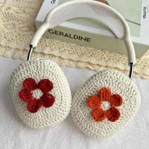 Puede incluir: Cubiertas de auriculares de crochet blanco con detalles de flores rojas y naranjas.