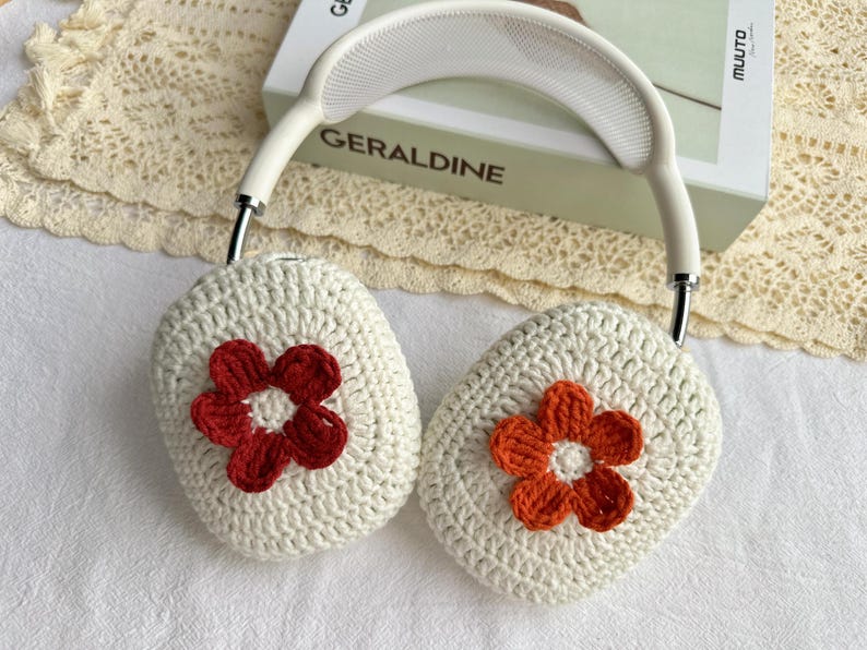 Puede incluir: Cubiertas de auriculares de crochet blanco con detalles de flores rojas y naranjas.