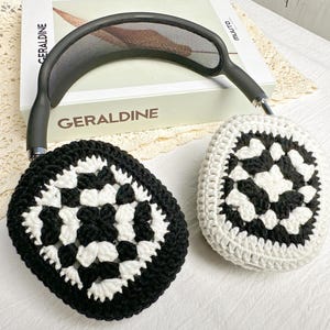 May include: Black and white crocheted earmuffs with a geometric pattern. The earmuffs are attached to a black headband.