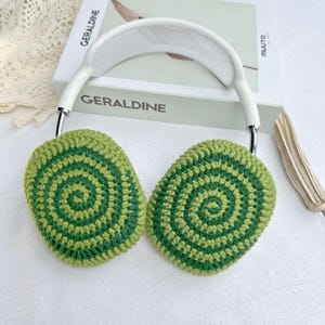 May include: White headphones with green and light green crocheted ear covers. The ear covers have a circular pattern.