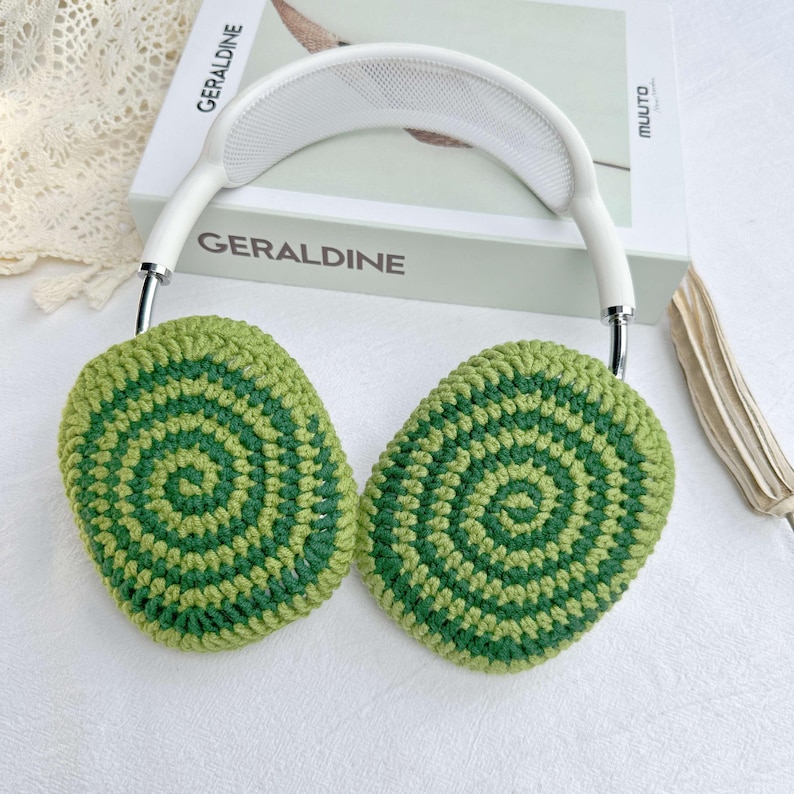 May include: White headphones with green and light green crocheted ear covers. The ear covers have a circular pattern.