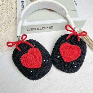 May include: Black crocheted headphone covers with red heart accents. The covers have a bow on each side.