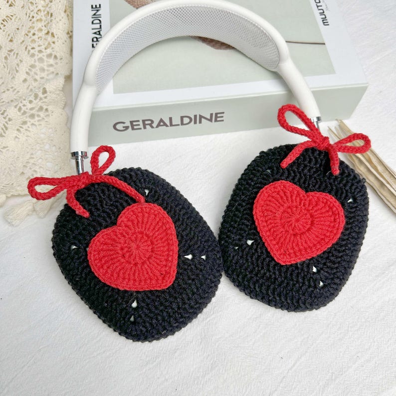 May include: Black crocheted headphone covers with red heart accents. The covers have a bow on each side.