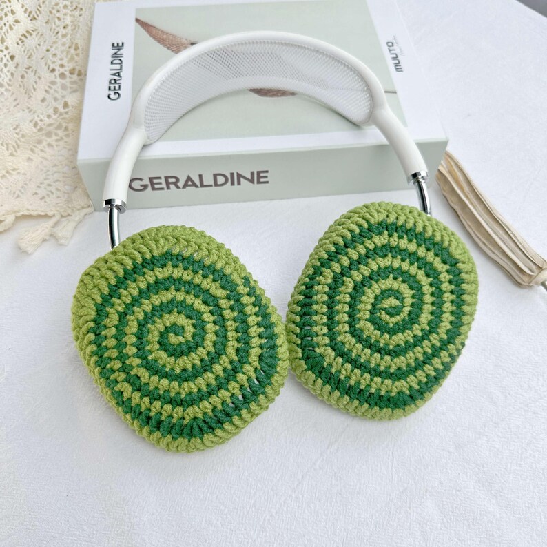 May include: Green and white crocheted earmuffs with a white headband. The earmuffs have a circular pattern.