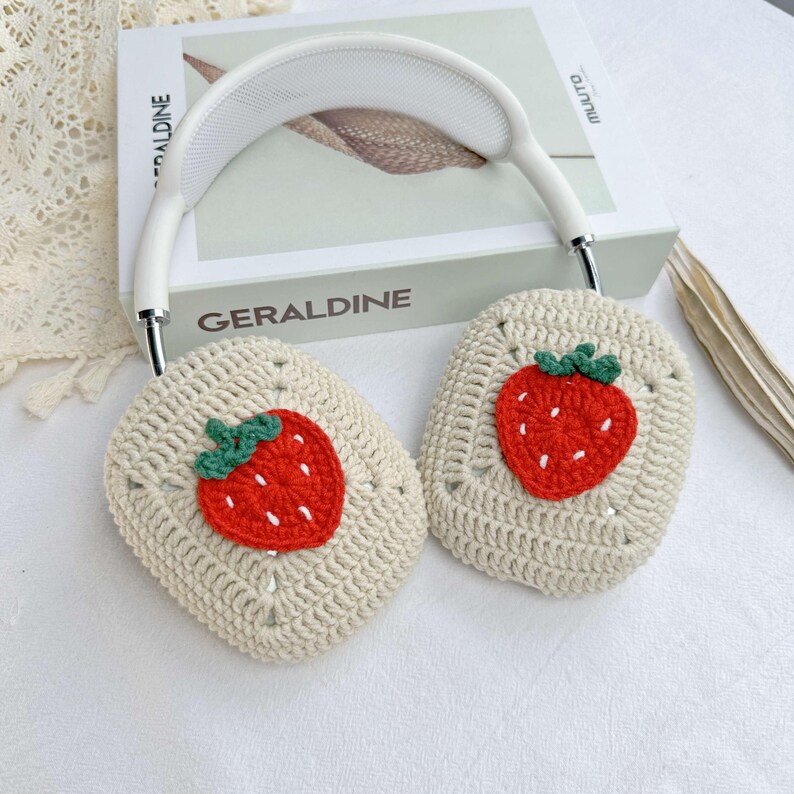 May include: White crocheted headphone covers with a strawberry design. The strawberries are red with green leaves and white stitching.