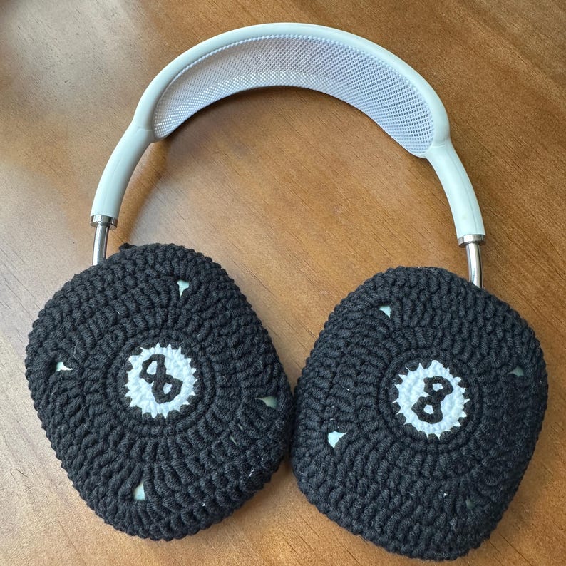 Puede incluir: Auriculares blancos con cubiertas de orejas de crochet negro. Las cubiertas de las orejas tienen un c&iacute;rculo blanco con el n&uacute;mero 8 en el centro.