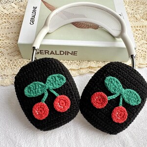 May include: Black crocheted earmuffs with a cherry design. The cherries are red with green leaves.