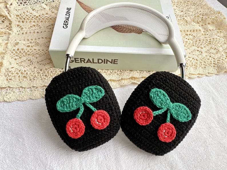 May include: Black crocheted earmuffs with a cherry design. The cherries are red with green leaves.