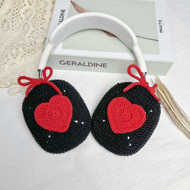 May include: Black crocheted earmuffs with red heart accents. The earmuffs are attached to a white headband.