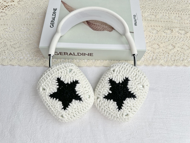 Puede incluir: Auriculares blancos con fundas de crochet con un dise&ntilde;o de estrella negra. Los auriculares descansan sobre un libro titulado "Geraldine". Las fundas son hechas a mano, agregando un toque art&iacute;stico &uacute;nico a los auriculares.