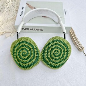 May include: Green and white crocheted earmuffs with a white headband. The earmuffs have a circular pattern.