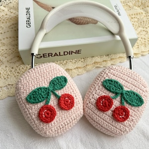 May include: A pair of pink crocheted earmuffs with a cherry design. The earmuffs are made of soft yarn and have a white headband.