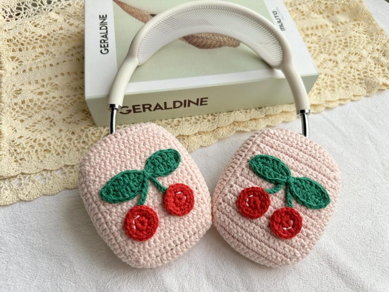 May include: A pair of pink crocheted earmuffs with a cherry design. The earmuffs are made of soft yarn and have a white headband.