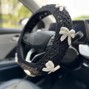 K&ouml;nnte beinhalten: Schwarze H&auml;kel-Lenkradabdeckung mit wei&szlig;en H&auml;kel-Schleifen.
