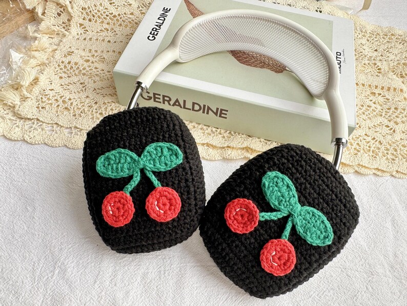 May include: Black crocheted headphone covers with a cherry design. The cherries are red with green leaves.