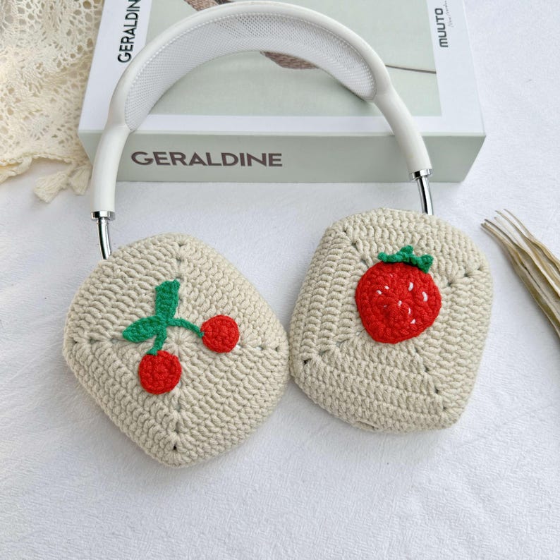 May include: White crocheted headphone covers with a strawberry and cherry design. The covers are made of a soft, beige yarn and feature embroidered fruit details.