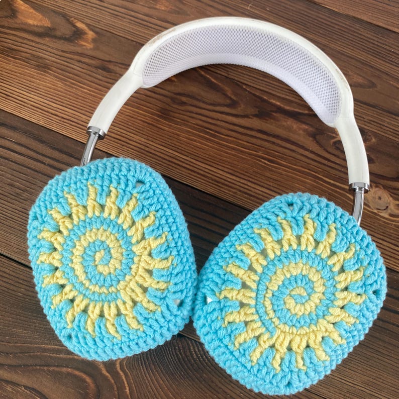 May include: White headphones with crocheted earmuffs. The earmuffs are blue and yellow with a sun design.