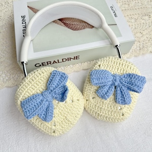 May include: A pair of crocheted ear warmers with blue bows. The ear warmers are cream coloured and the bows are a light blue.