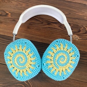 May include: White headphones with crocheted earmuffs. The earmuffs are blue and yellow with a sun design.