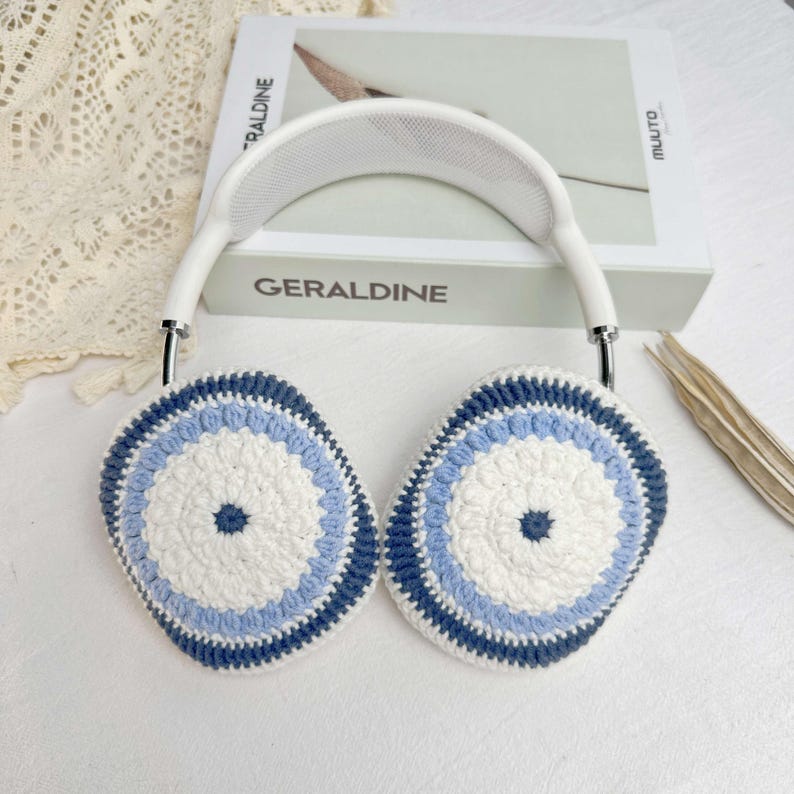 Puede incluir: Orejeras de crochet blanco con rayas azules y azul claro. Las orejeras son redondas y tienen una diadema blanca.