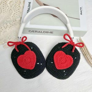 May include: Black crocheted headphone covers with red heart accents and white bows. The covers are attached to a white headband.