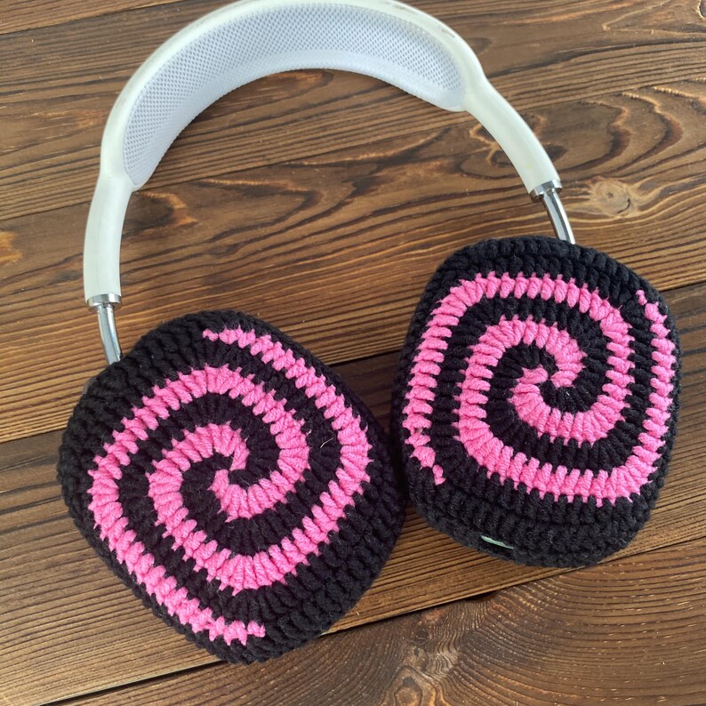 May include: Black and pink crocheted earmuffs with a spiral pattern. The earmuffs are attached to a white headband.