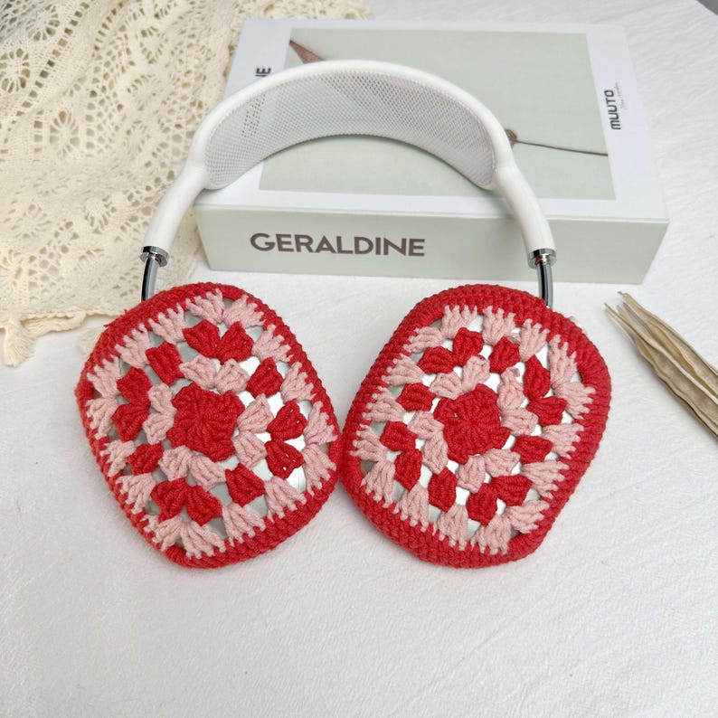 Op de afbeelding: Rode en roze gebreide oorkappen met een witte hoofdband. De oorkappen hebben een granny square patroon.