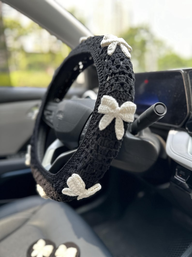 K&ouml;nnte beinhalten: Schwarze H&auml;kel-Lenkradabdeckung mit wei&szlig;en H&auml;kelblumen-Akzenten.