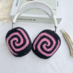 May include: Pink and black crocheted earmuffs with a spiral pattern. The earmuffs are attached to a white headband.