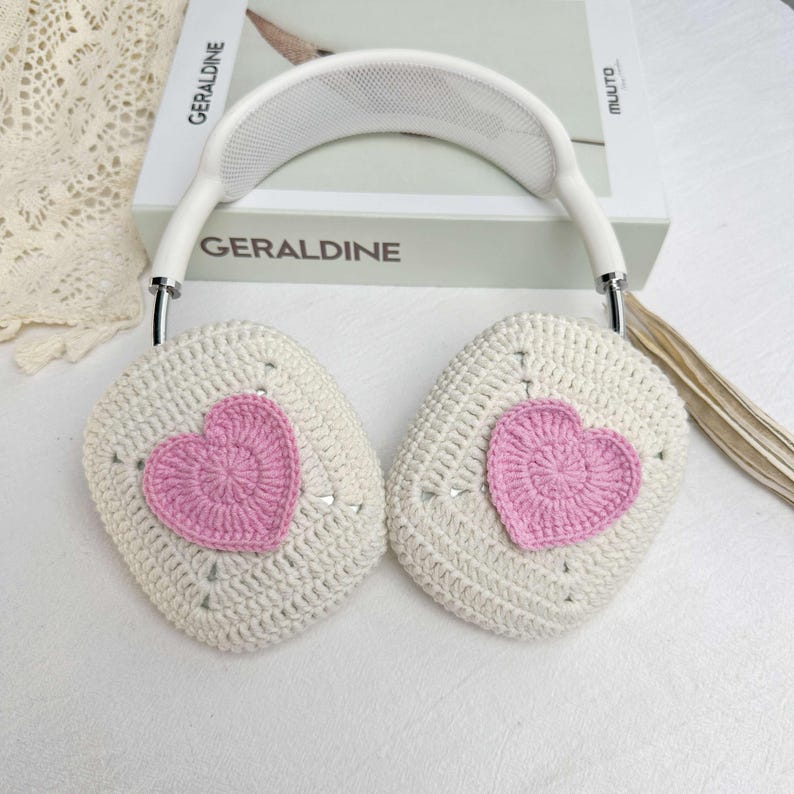 May include: White crocheted earmuffs with pink heart-shaped crochet embellishments. The earmuffs are attached to a white headband with a mesh design.