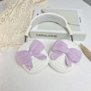 Puede incluir: Orejeras de crochet blanco con lazos de color lavanda. Las orejeras est&aacute;n unidas a una diadema blanca.