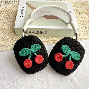 May include: Black crocheted headphone covers with a cherry design. The cherries are red with green leaves.