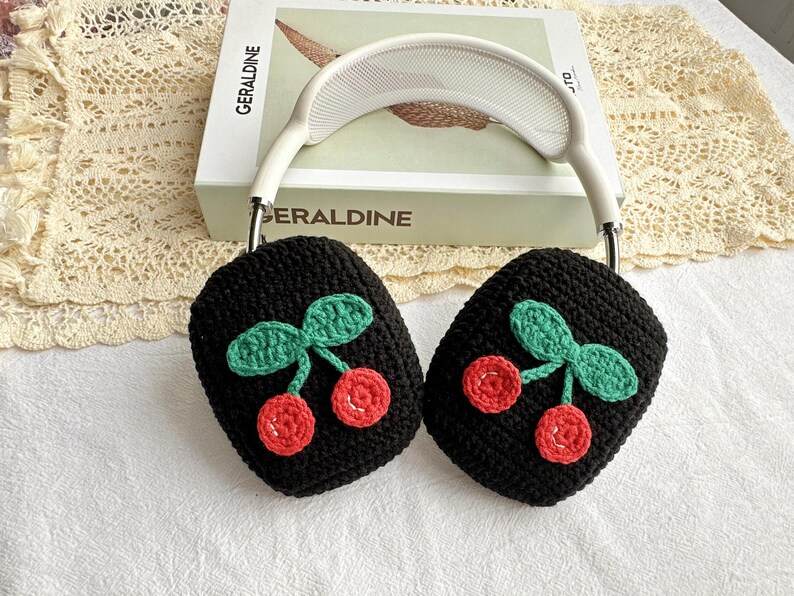 May include: Black crocheted headphone covers with a cherry design. The cherries are red with green leaves.