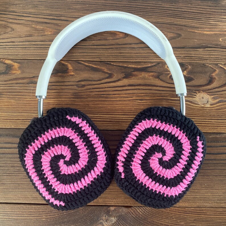 May include: White headphones with black and pink crocheted earmuffs featuring a spiral pattern.