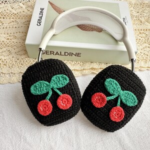 May include: Black crocheted headphone covers with a cherry design. The cherries are red and green.