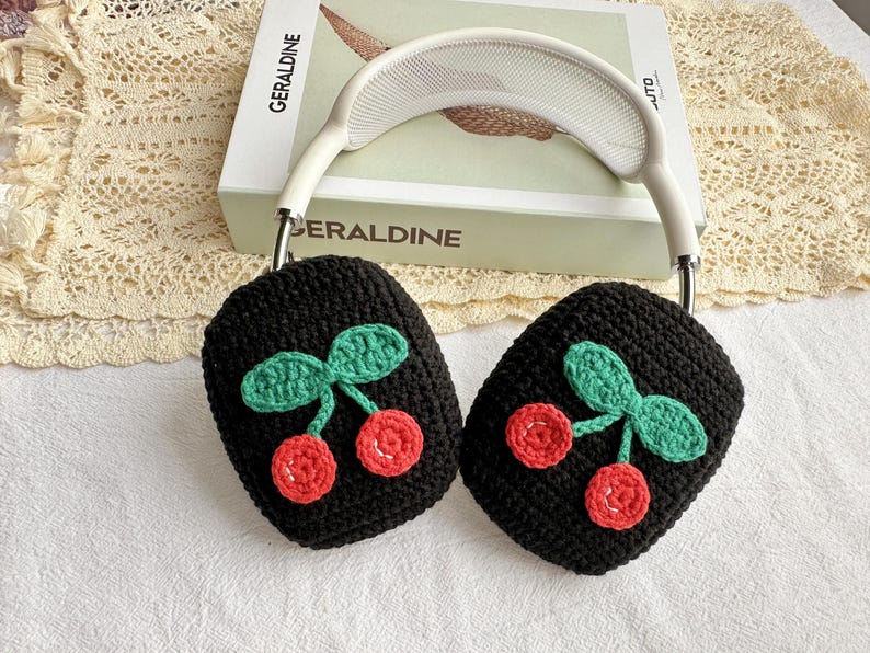 May include: Black crocheted headphone covers with a cherry design. The cherries are red and green.