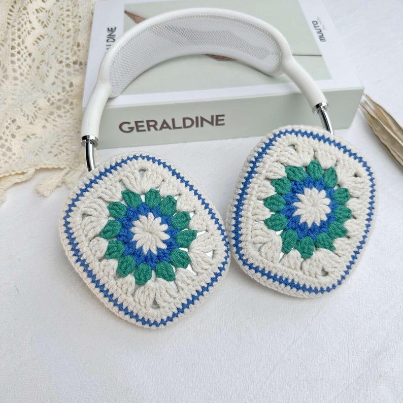 May include: White headphones with crocheted ear covers. The ear covers are white with blue and green accents and feature a floral design.