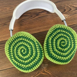 May include: Green and lime green crocheted earmuffs with a white headband. The earmuffs have a circular pattern.
