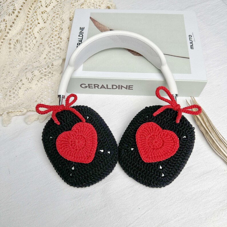 May include: White headphones with black and red crocheted earmuffs. The earmuffs have a heart shape with a red crocheted center.