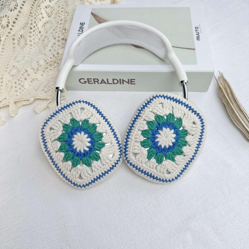 May include: White crochet earmuffs with a blue and green floral pattern. The earmuffs are attached to a white headband.
