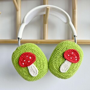 May include: White headphones with green crocheted earmuffs featuring red and white mushroom appliques.