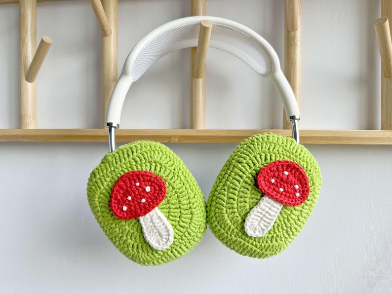 May include: White headphones with green crocheted earmuffs featuring red and white mushroom appliques.