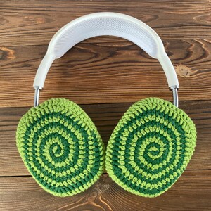 May include: Green and white crocheted earmuffs with a white headband. The earmuffs have a circular pattern.