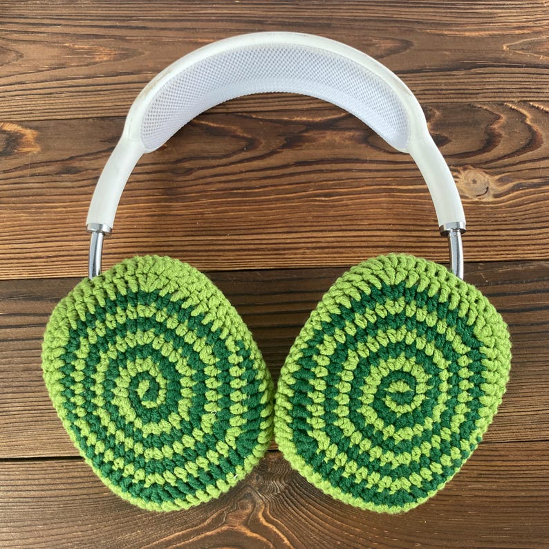 May include: Green and white crocheted earmuffs with a white headband. The earmuffs have a circular pattern.